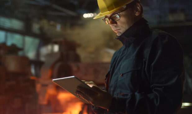 man in a hardhat using an ipad in an industrial setting